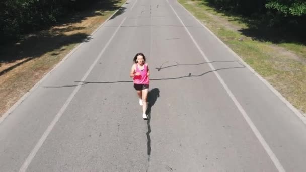 Молода струнка жінка бігунка в рожевому спортивному одязі тренується в зеленому міському парку. Навчання важке. Спортивна приваблива дівчина в навушниках тренується в парку . — стокове відео