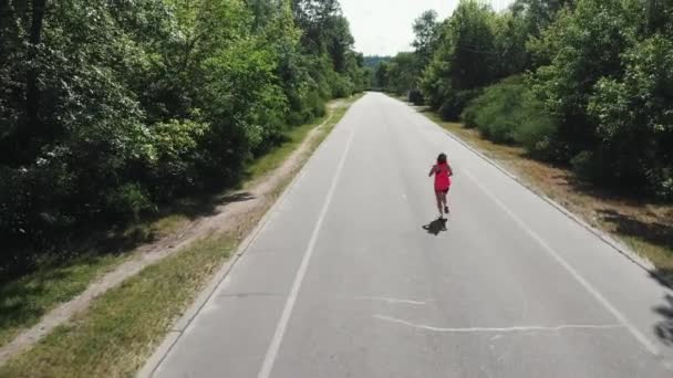 Joven chica atractiva con el cuerpo entrenado se está ejecutando en el día caliente. Mujer deportiva delgada en rosa entrenamiento superior en el parque verde de la ciudad. Hermosa corredora. Ejecutar entrenamiento — Vídeo de stock