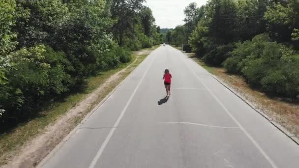 Belle coureuse sportive en casque et chemise rose s'entraîne dans le parc de la ville. Slim brune femme caucasienne court. Fille attrayante dans des écouteurs avec un corps formé. Entraînements de course — Video