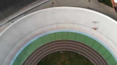 Velodrome'da eğitim gören güçlü bisikletçilerin drone görüntüsünü kapatın. Bisiklet pistinde bisiklete binen genç kız. Velodrome'da bisikletçilerin drone üst görünümü