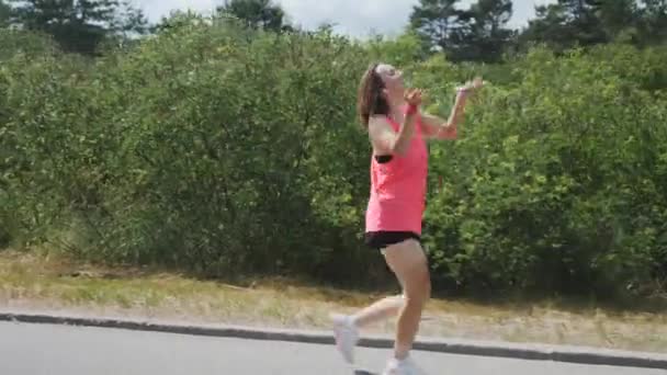 Chica atractiva con un bronceado divertido. Mujer joven y deportiva bailando en el parque. Chica morena se divierte en el parque. Mujer con camisa rosa en auriculares escuchando música — Vídeos de Stock