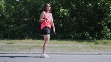 Parkta dans eden kulaklıklı genç, çekici beyaz kız. Sportif kadın komik hareketler yapıyor ve eğleniyor. Parkta gülünç hareketler yapan pembe gömlekli kız