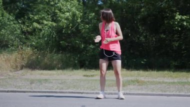 Kulaklık dans ve parkta eğlenmek Ince güzel kız. Parlak spor giyimgenç kadın garip komik hareketler yapıyor ve etrafında şaka. Sevimli kız gülümsüyor ve gülüyor. Yavaş çekim