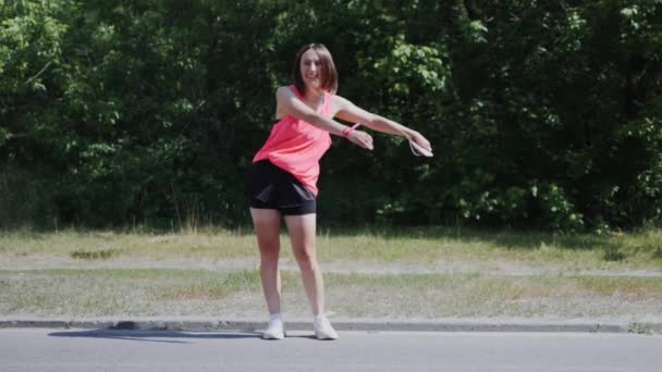 Giovane ragazza sportiva danza zaino bambino danza nel parco. Attraente ragazza in cuffia che esegue danza filo interdentale nel parco. Ragazza che si diverte al parco. Bella ragazza che cerca di far ballare il filo interdentale. Rallentatore — Video Stock