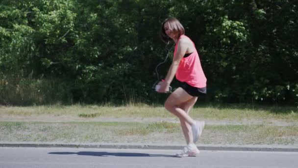 Menina branca em fones de ouvido dançando no parque. Menina atraente fazendo movimentos engraçados e se divertindo. A rapariga gira está a brincar. Mulher bonita a fazer dança engraçada. Movimento lento — Vídeo de Stock