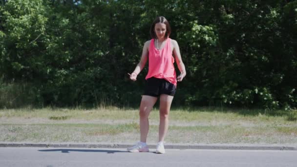 Kaukasiska ung flicka i hörlurar gömmer smartphone. Attraktiv Sportiv tjej som har kul i parken. Slow motion — Stockvideo
