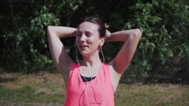 Kulaklık dans ve şarkı şarkı genç sıcak çekici kız. İnce sportif kadın parkta müzik dinliyor. Kız sıcak yaz gününde parkta duruyor. Genç kız koşudan sonra zevk alıyor