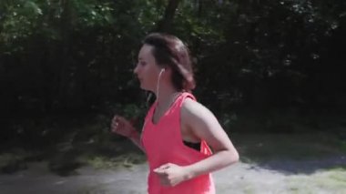 Kulaklık ile parlak pembe üst Çekici ince kız eğitim sırasında ağır nefes alıyor. Parkta koşan genç sportif kadın. Şehir parkında kız eğitimi. Çalışan egzersizler yapan kadın