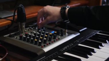 Müzik yapımcısı mühendis ekolayzır ile karıştırma tahtası üzerinde knobs döner. Ev stüdyosu kayıt karıştırma ve mastering süreci. Elektronik midi piyano ve karıştırma tahtası. Ev kayıt müzik stüdyosu.