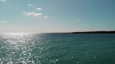 Kıbrıs Mercan Plajı'nda güneş yolu ve kayalık tükürük yarımadası ile mavi Akdeniz ve gökyüzü. Güneş yansıması ile mavi deniz ve gökyüzü havadan görünümü. Okyanusun drone görünümü.
