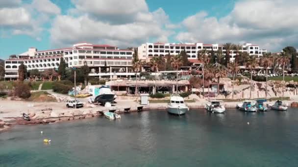 Chipre restaurante do hotel e barcos brancos na marina do mar na praia da baía de coral. Vista aérea do hotel e dos navios de cruzeiro que descansam perto do cais do mar. Disparo de drone. Coral Bay em cyprus no dia ensolarado ventoso — Vídeo de Stock