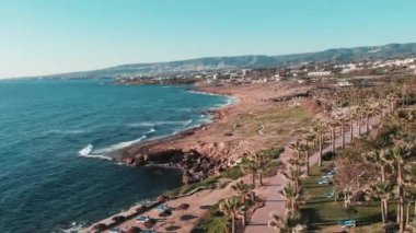 Palmiye, otel ve tatil alanı ile Kıbrıs'ta mercan körfezi kayalık sahil in üst görünümü. Güçlü deniz dalgaları kayalık sahile çarparak beyaz köpük ve sıçrama yaratıyor. Deniz kayalık plaj havadan çekim