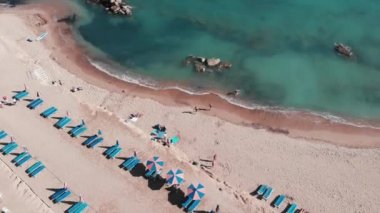 Sahilde yatan insanları drone atışı. Yüzme kıyafeti giyen insanlar güneşleniyor. Bikinili kızlar deniz kıyısında dinleniyor. Beyaz kum ve masmavi deniz suyu ile plajın havadan üst görünümü