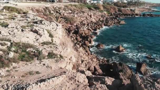 Orilla rocosa con fuertes olas tormentosas golpeando acantilados y salpicaduras. Aerial drone shot of coral rocky beach with waves coliding with rocks creating white foam . — Vídeo de stock