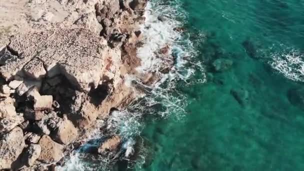 Drone lövés alatt tiszta átlátszó tenger hullámai találkozó sziklás strand sziklák fröccsenő és megteremti fehér hab. Légi kilátás az óceán erős hullámok sújtotta sziklás tengerpart a fröccsenő és fehér hab — Stock videók