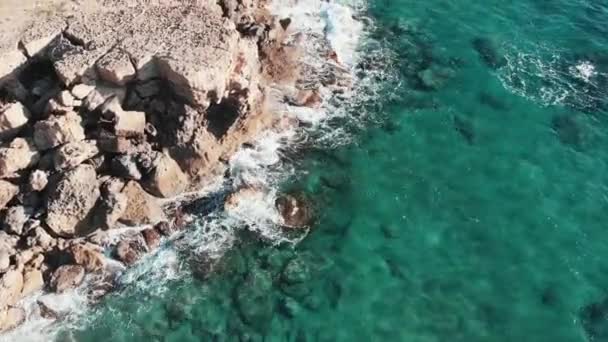 Drone flies over seashore. Rocky cliffs and seashore with strong ocean stormy waves colliding together creating white foam and splashing everywhere. Aerial top view of blue water and cliffs — Stock Video