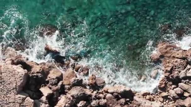无人机沿着岩石海滩飞行。美丽的海岸线与波浪。大海岩石的鸟瞰图。大浪冲击海岸的顶视图。强大的海浪冲击岩石。波浪飞溅和产生泡沫 — 图库视频影像