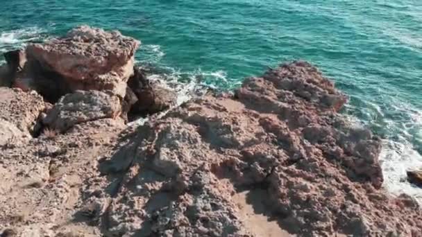 岩の海岸の航空写真。アズール海水で美しい海岸線。崖に当たる海の波。海の波が飛び散り、泡を作り出します。海の大きな岩のドローンショット。青い澄んだ海の波 — ストック動画