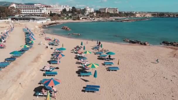 Piaszczysta plaża z parasolami i leżakami. Rodzina na wakacjach. Dziewczęta i chłopcy leżący na plaży. Dron leci przez piaszczystą plażę. Ludzie relaksując się w letni dzień. Widok z lotu ptaka na brzeg morza. — Wideo stockowe