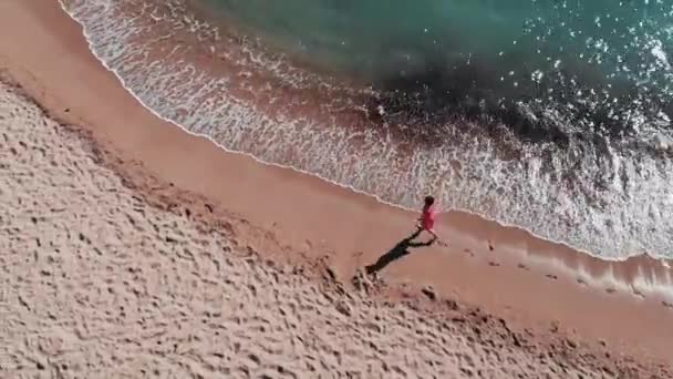 Jong meisje op Sandy kust. Meisje laat voetafdrukken op zand. Aantrekkelijke vrouw in rode jurk op het strand. Meisje wandelen langs de kust. Luchtfoto van de kust. Prachtige oceaan golven. Strand met wit zand — Stockvideo