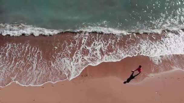 Dziewczyna na plaży. Kobieta w czerwonej sukni chodzenie na piaszczystej plaży. Młoda atrakcyjna dziewczyna chodzenie w dół plaży. Widok z lotu ptaka na piaszczystą plażę. Niebieski krystalicznie czyste wody morskiej. Drone leci przez piękną plażę. — Wideo stockowe
