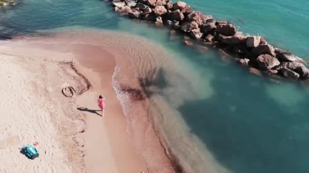 Привлекательная женщина в красном платье на пляже. Молодая девушка гуляет по пляжу. Вид с воздуха на прекрасный песчаный пляж с голубой чистой водой. Леди в красном платье на берегу моря. Беспилотник летит вдоль прекрасного пляжа — стоковое видео