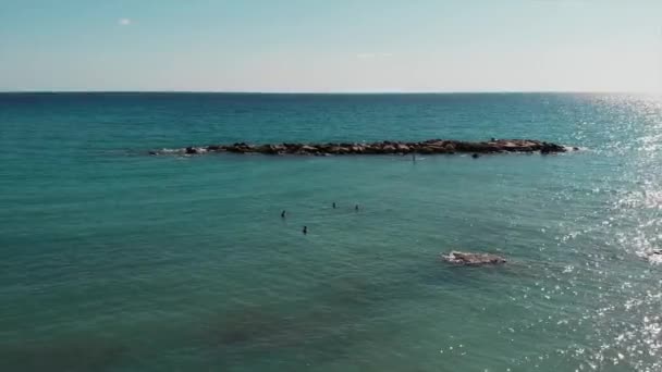 Drone kayalık deniz kıyısına yakın uçuyor. Mavi deniz suyunun havadan görünümü. Güzel deniz manzarası. Sup genç çekici adam. Güneş tabaklanmış çocuk sup üzerinde yüzen. Mutlu erkekler yüzme ve güneşin tadını çıkarıyor — Stok video