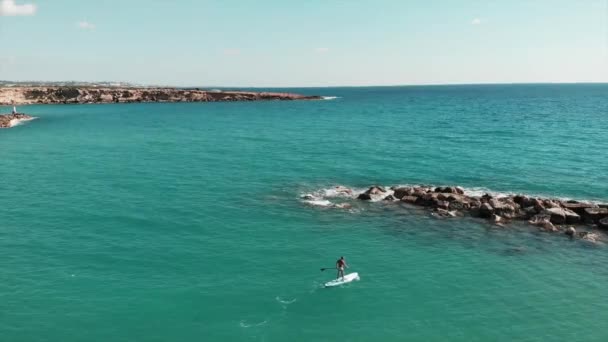 Kayalık taşlar boyunca yüzen sup üzerinde şort sportif güneş tabaklanmış çocuk. Güzel deniz manzara havadan drone görünümü. Kayalık sahildedrone fotoğrafı. Mavi berrak su ile Akdeniz'in havadan görünümü — Stok video