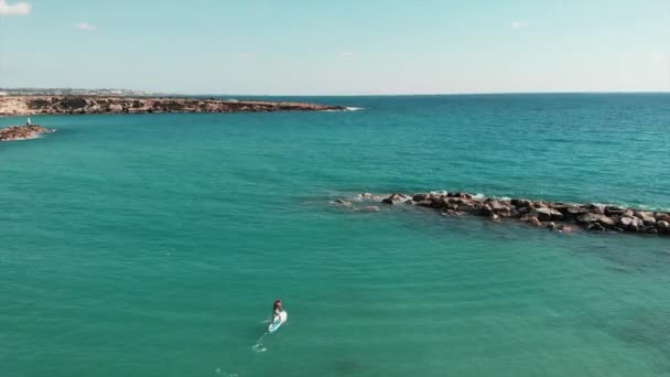 Aerial view of blue crystal clear sea water. Drone shot of beautiful rocky coastline. Young attractive man on sup floating along rocky seashore. Aerial shot of beautiful sea landscape — Stock Video