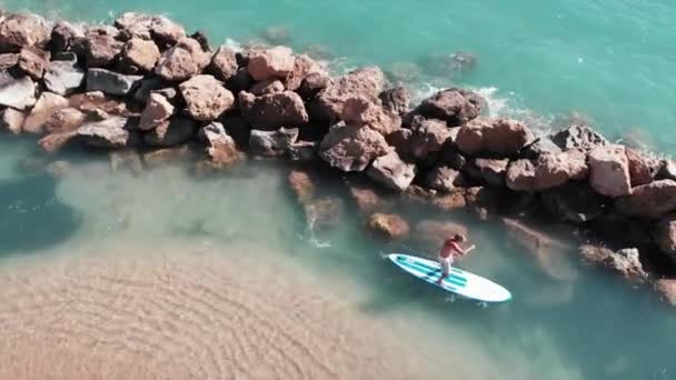 Attractive sun-tanned boy on sup. Aerial view of sportive man floating on sup. Drone shot of crystal clear sea water. Young boy surfing near sandy beach — Stock Video