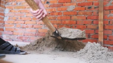 Kürek kazma kumu. Elelinde kürek kırmızı tuğla duvara yakın kum kazmak. İnşaat konsepti