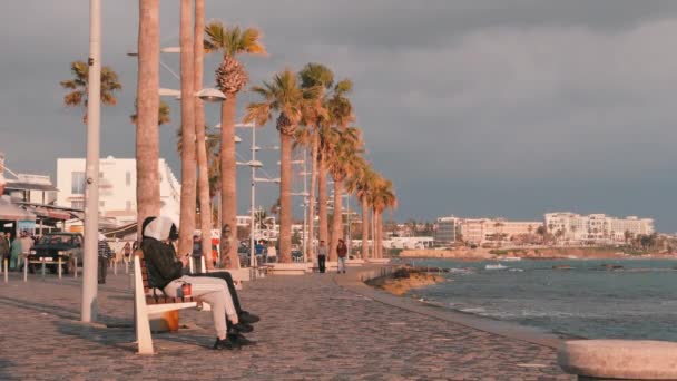 Mars, 16, 2019 / Chypre, Paphos Promenade touristique à Paphos, Chypre. Des gens marchent sur le quai. Sentier pédestre avec des gens relaxants sur le littoral. Groupe de personnes se relaxant sur le quai. Espace touristique avec cafés et restaurants. Mouvement lent — Video