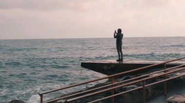 Genç çocuk yağmurlu denizin videosunu çekiyor. Gezinti yerinde fotoğraf yapan çekici adam. Fırtınalı denizin resimlerini yapan yalnız çocuk. Okyanusa bakan melankolik genç çocuk