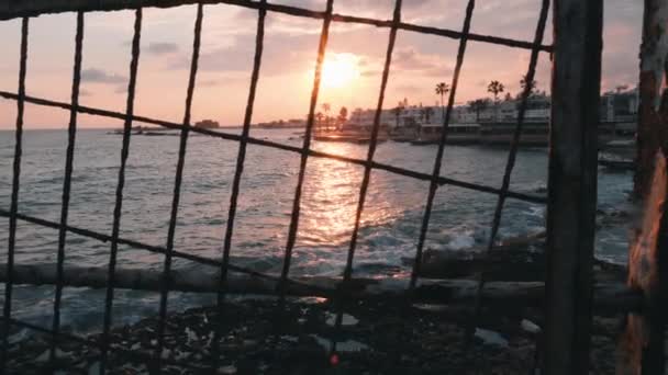 Hermosa puesta de sol a través de celosía. Puesta de sol rosa en la zona turística. Puesta de sol en la costa. Paseo marítimo al atardecer. Zona turística peatonal al atardecer. Puesta de sol en zona turística. Puesta de sol con edificios. Movimiento lento — Vídeos de Stock