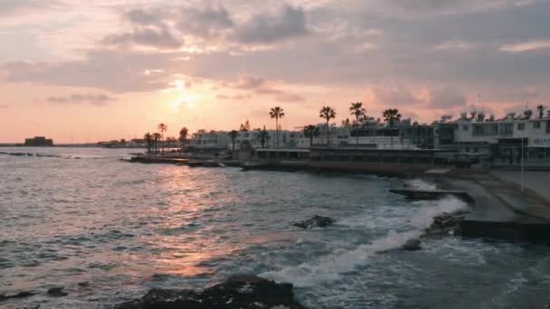 Puesta de sol rosa en el puerto deportivo. Hermosa zona peatonal al atardecer. Paseo turístico con palmeras. Grandes olas oceánicas se estrellan en el muelle al atardecer. Zona turística con hoteles. Gente caminando en el muelle . — Vídeos de Stock