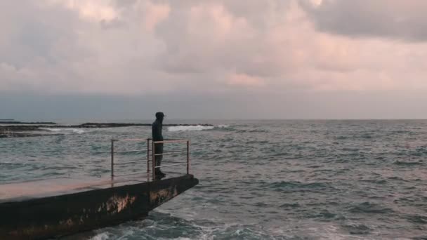 Widok z boku samotny chłopiec patrząc na burzą ocean. Młody smutny chłopiec patrząc na horyzoncie. Melancholy chłopiec stoi na molo. Młody samotny człowiek w opuszczonych Seacoast. Zwolnionym — Wideo stockowe