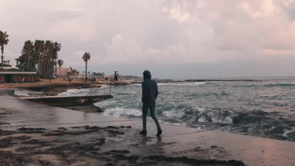 Un joven solitario caminando por la costa desierta. Hombre melancólico caminando por el paseo marítimo. El joven está triste. Mal tiempo tormentoso en el paseo de la ciudad. Paseo marítimo en la tormenta . — Vídeos de Stock