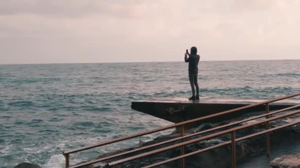 어린 소년 촬영 비디오 의 비오는 바다 산책로에서 사진을 만드는 매력적인 남자. 폭풍우 바다의 사진을 만드는 외로운 소년. 바다를 바라보는 우울한 어린 소년 — 비디오