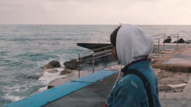 Tæt på udsigt over ensom pige på Marina. Melankolsk pige kigger på stormfulde hav. Pessimistisk ung kvinde i afslappet stil stående ved promenaden. Nærbillede af trist melankolsk kvinde – Stock-video