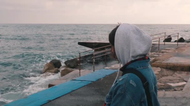 바닷가에 서 있는 우울한 소녀. 폭풍우 바다를 바라보는 외로운 여자. 슬픈 소녀의 보기를 닫습니다. 산책로에 서있는 어린 소녀. — 비디오