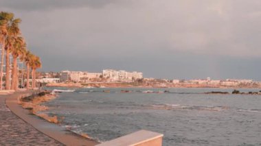Baf rıhtımı. Kıbrıs'ta turist gezinti. Pembe alacakaranlıkta turist bölgesi. Rocky Beach boyunca çekici erkek koşucu eğitim. Akdeniz kıyıları. Arka planda oteller ile Fırtınalı deniz
