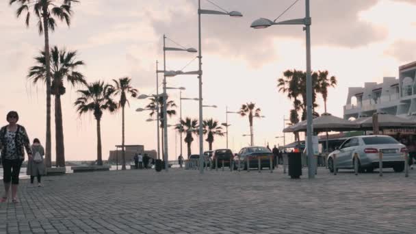 Marzo, 16, 2019 / Chipre, Paphos Hermoso muelle con coches y sendero peatonal. Turistas caminando en el paseo marítimo en Paphos, Chipre. Paseo turístico con palmeras. Zona turística con cafeterías y tiendas — Vídeo de stock