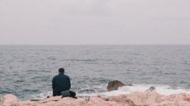 Office worker came to seacoast to have lunch. Lonely office worker having lunch by rocky beach. Man having lunch out of office. Melancholy man looking at stormy sea. Lamentable boy sitting at sea