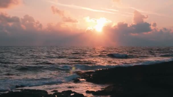 ピンクの夕日と岩のビーチで美しいロマンチックな夜。雲と信じられないほどのピンクの空。地中海の日没。日没の美しいピンクの光線。地平線上にピンクの空と嵐の海 — ストック動画