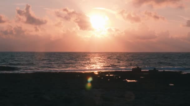 ピンクの夕日に対する岩のビーチの美しい景色。岩のビーチのピンクの夕日。太陽が地平線に沈む。夕日の信じられないほどのピンクの光線。海のピンクの日没 — ストック動画
