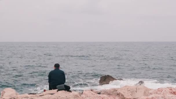 Büroangestellte kamen an die Küste, um zu Mittag zu essen. einsame Büroangestellte beim Mittagessen am felsigen Strand. Mann beim Mittagessen aus dem Büro. Melancholischer Mann mit Blick auf stürmische See. Bedauernswerter Junge sitzt auf See — Stockvideo