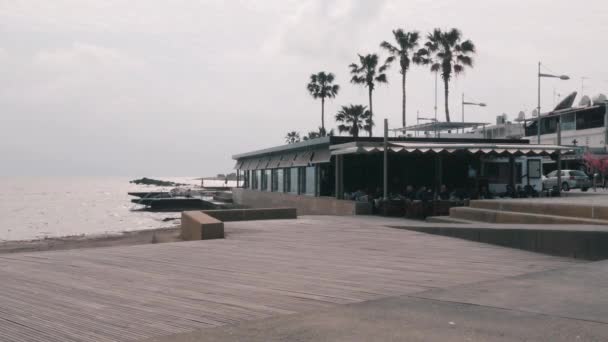 16 de marzo de 2019 / Chipre, Paphos. Timelapse de zona turística con restaurantes y palmeras. Turistas relajándose en la playa restaurante timelapse material de archivo. Timelapse de muelle con gente caminando por la playa — Vídeo de stock