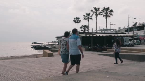 16 de marzo de 2019 / Chipre, Paphos. Restaurante de playa con gente que se relaja en terraza de verano. Turistas caminando por la playa. Hermoso muelle con mar . — Vídeos de Stock