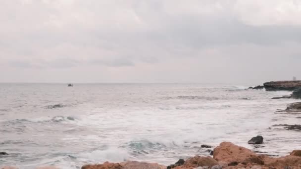 De grosses vagues océaniques s'écrasent sur une plage rocheuse. Belle vue sur la mer Méditerranée avec plage de rochers. Océan orageux venteux avec de grandes vagues. Grandes vagues orageuses balancent un petit bateau de pêche — Video