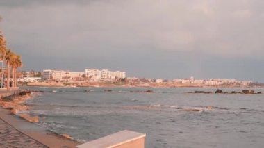 Gün batımında kayalık sahil. Gezinti yolunda koşan genç bir adam. Pembe alacakaranlıkta yaya yolu. Pembe alacakaranlıkta baf iskelesi. Ufukta oteller ile Fırtınalı okyanus dalgaları. Otellerle turist hattı. Turist rıhtımı